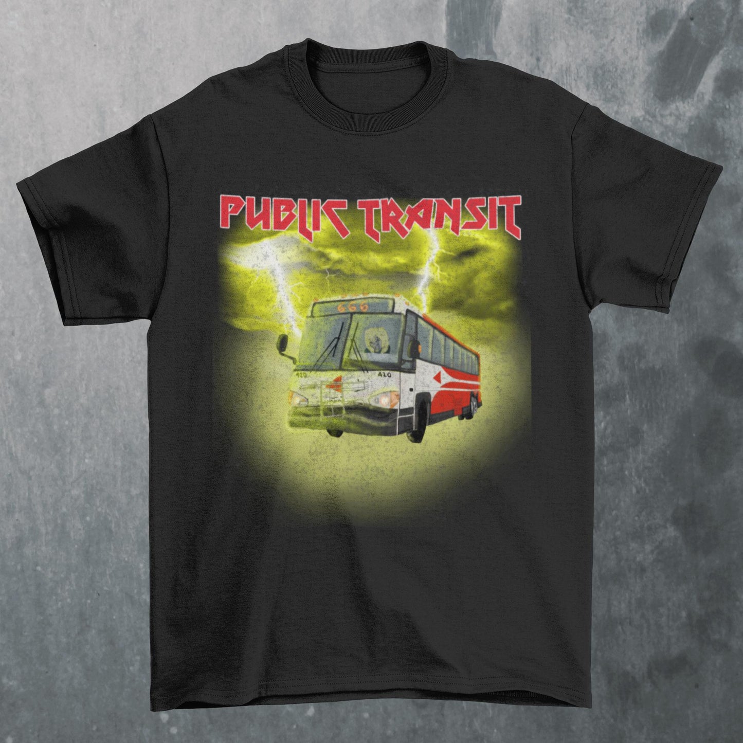 black t-shirt laying flat with the words public transit in red metal band font and a red city bus with a skeleton driver and the route number 666 all surrounded by glowing yellow clouds and lightning