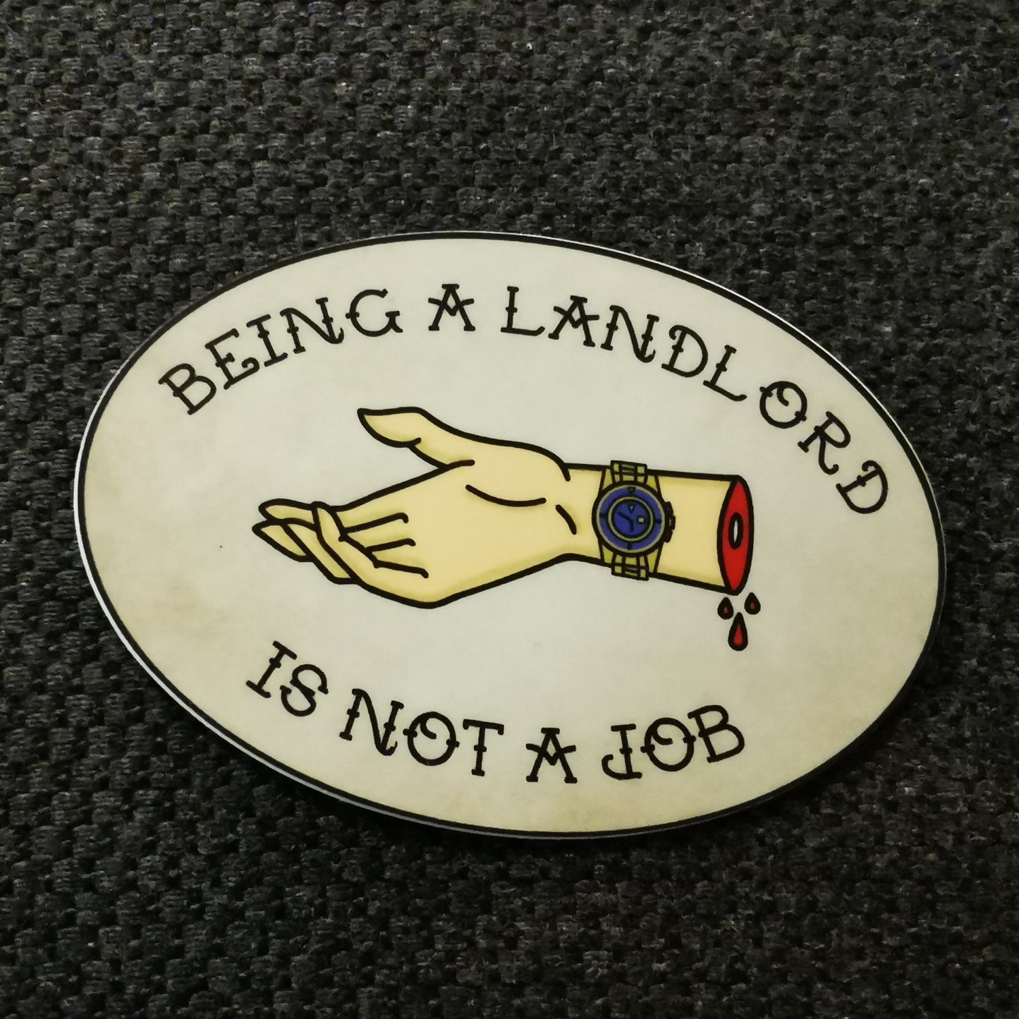 oval sticker with an old stained paper kind of background and the words "being a landlord is not a job" in an all-caps traditional tattoo font and a severed hand dripping blood outstretched for your rent wearing a fancy gold watch