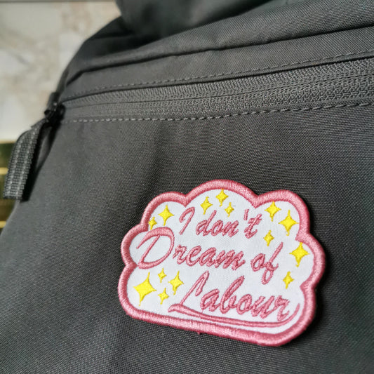 pink lined cloud with yellow stars and cursive text reading "i dont dream of labour" iron-on patch on a grey backpack 