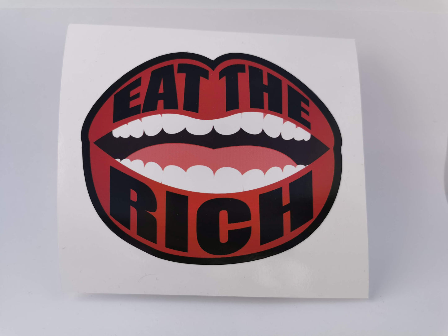 an open mouth with a black border and black text on the red lips that reads "eat the rich"