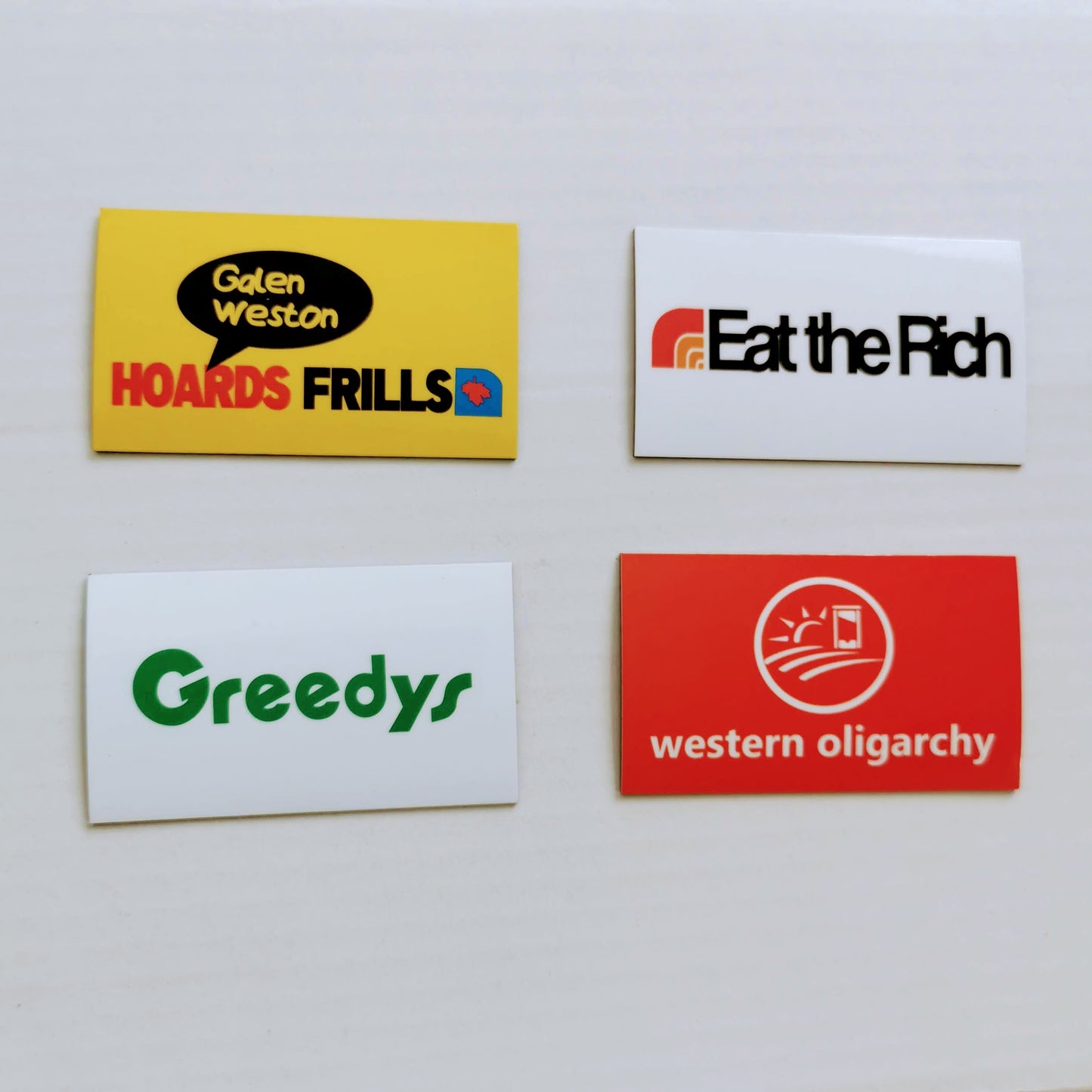 4 magnets on a white background. Galen Weston hoards frills , eat the rich, greedys, and western oligarchy. Each magnet is designed to look like a different major canadian grocery retailer.