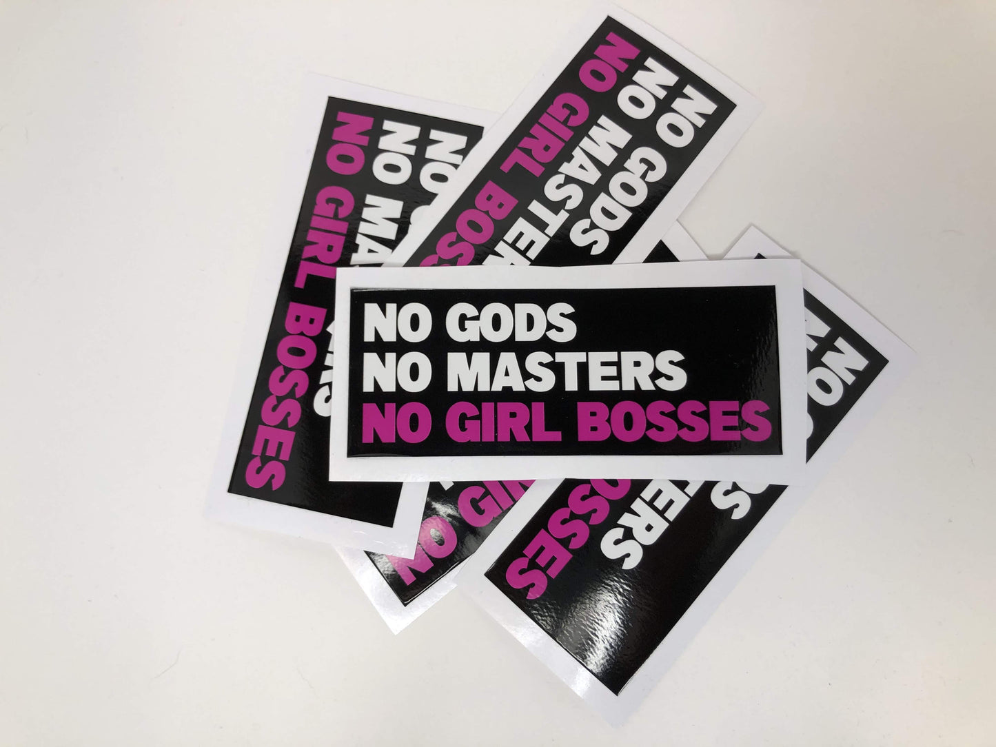 A black rectangle with the words "no gods no masters" in white and "no girl bosses" in pink